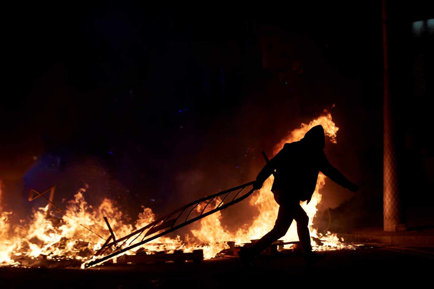 Un manifestante lanza una valla a la barricada en llamas en la calle Aragó, anoche en Barcelona durante las protestas por la detención de Pablo Hasél.