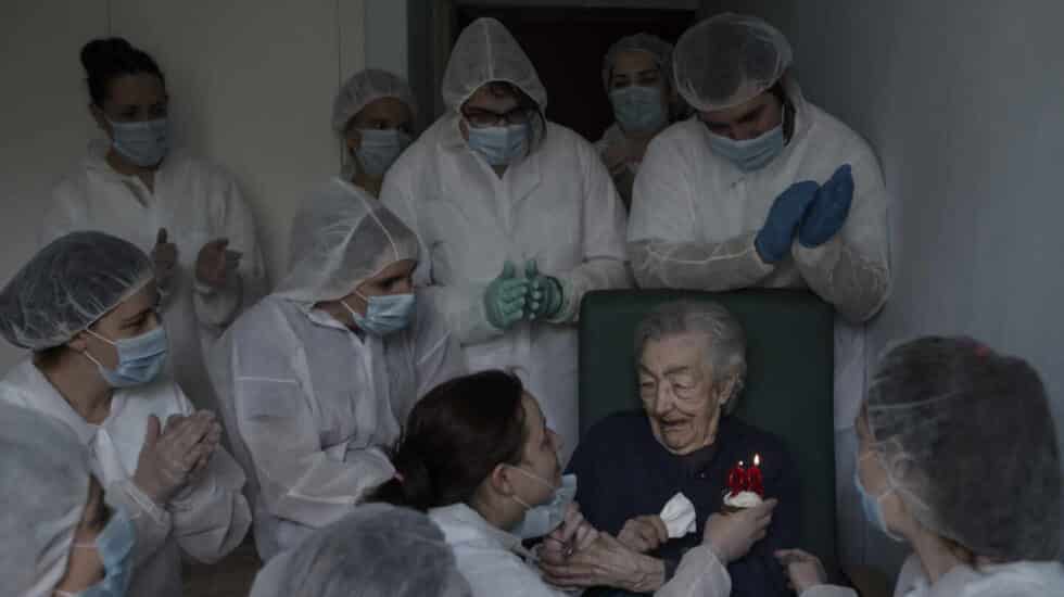 Señora mayor con Covid en una residencia soplando las velas por su cumpleaños junto a los sanitarios equipados con EPIs