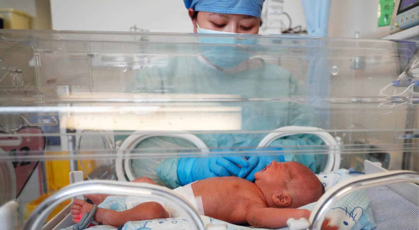 Un bebé recién nacido dentro de una cuna en cuidados intensivos de neonatos atendido por una enfermera