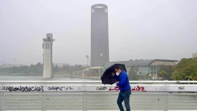 Un persona se protege de la lluvia y el viento caminando por Sevilla.