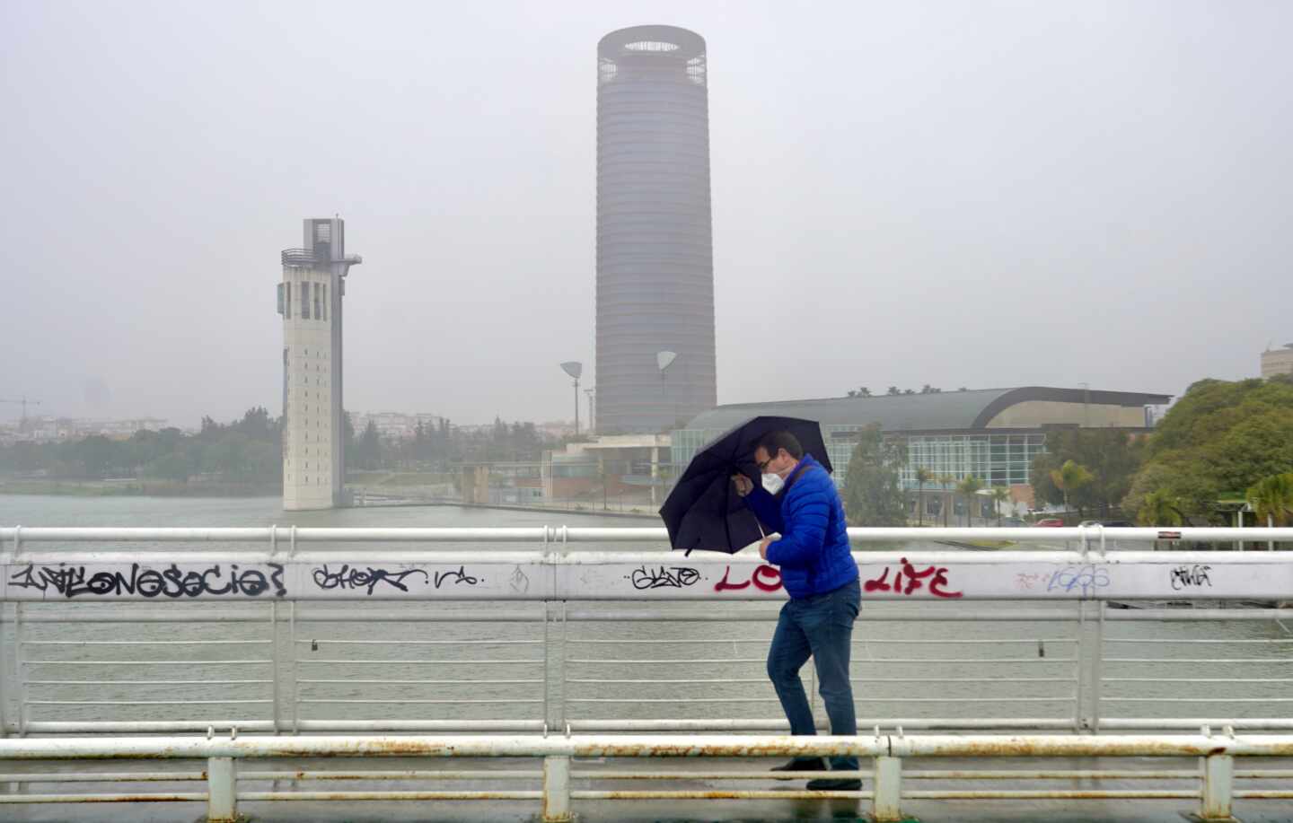 Un persona se protege de la lluvia y el viento caminando por Sevilla.