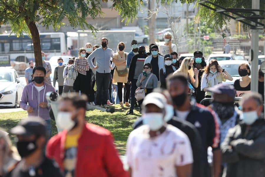 Extranjeros residentes en Israel hacen cola para recibir la vacuna de Pfizer.