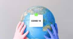 Dos manos con guantes sujetan un globo terráqueo con una nota en la que se lee "Covid-19".