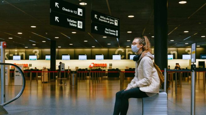 Una chica sentada sobre su maleta espera en un aeropuerto.