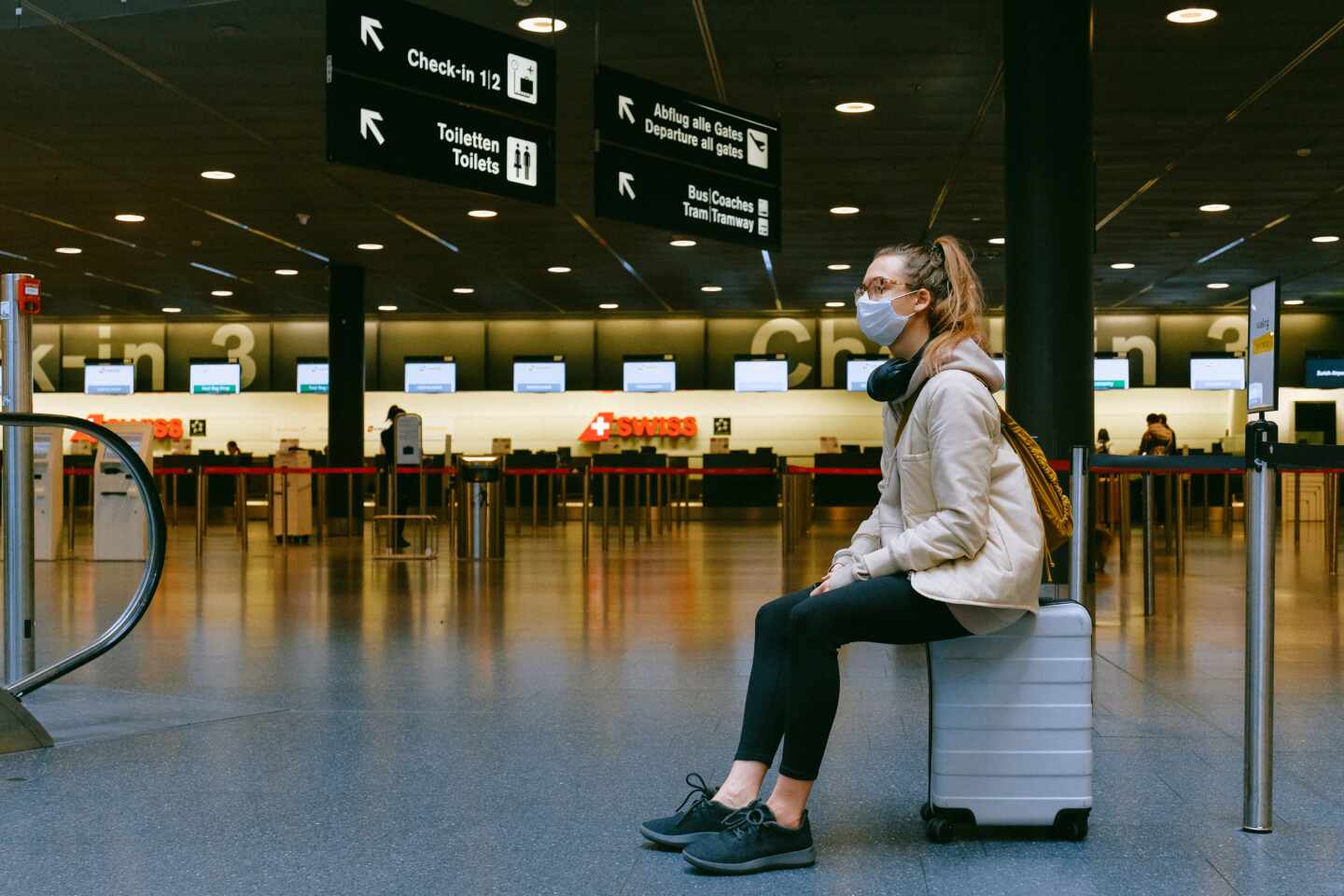 Una chica sentada sobre su maleta espera en un aeropuerto.