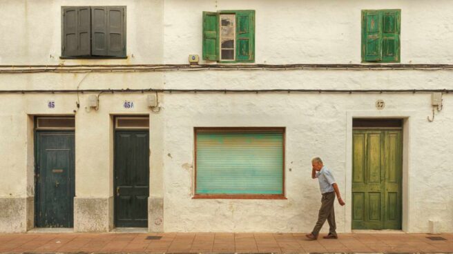 Un hombre de edad avanzada pasea frente a unas casas viejas.
