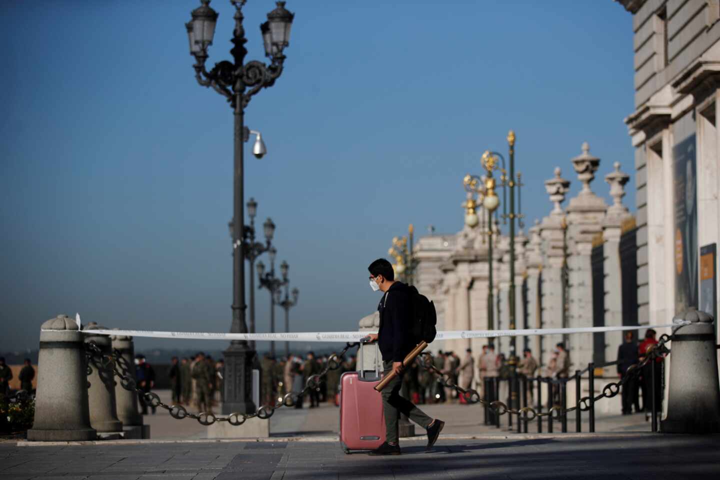 Un joven con su maleta pasa ante el Palacio Real de Madrid.