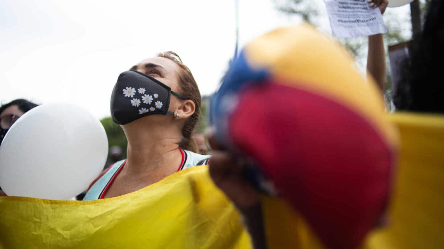 Una mujer manifestándose contra el abuso sexual sosteniendo una pancarta con una mascarilla y mirando al aire