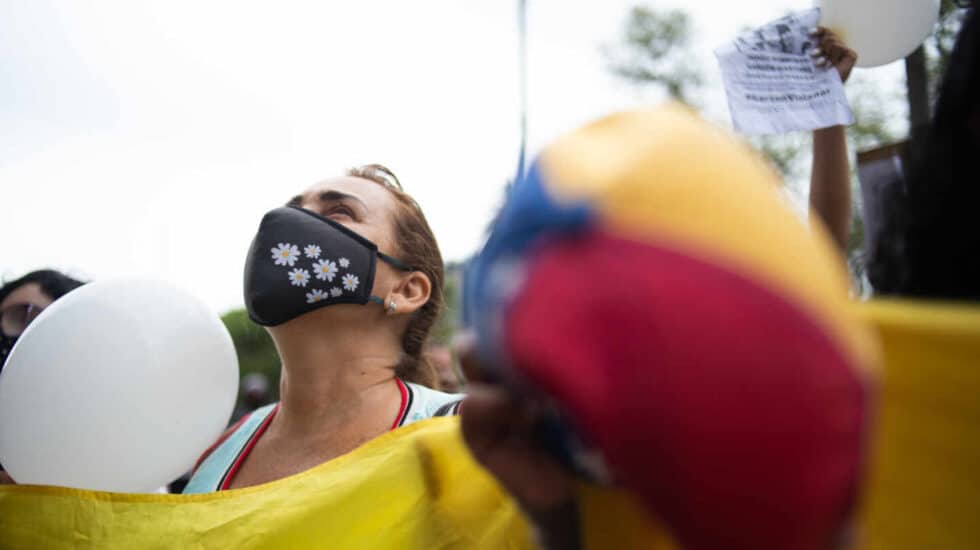Una mujer manifestándose contra el abuso sexual sosteniendo una pancarta con una mascarilla y mirando al aire
