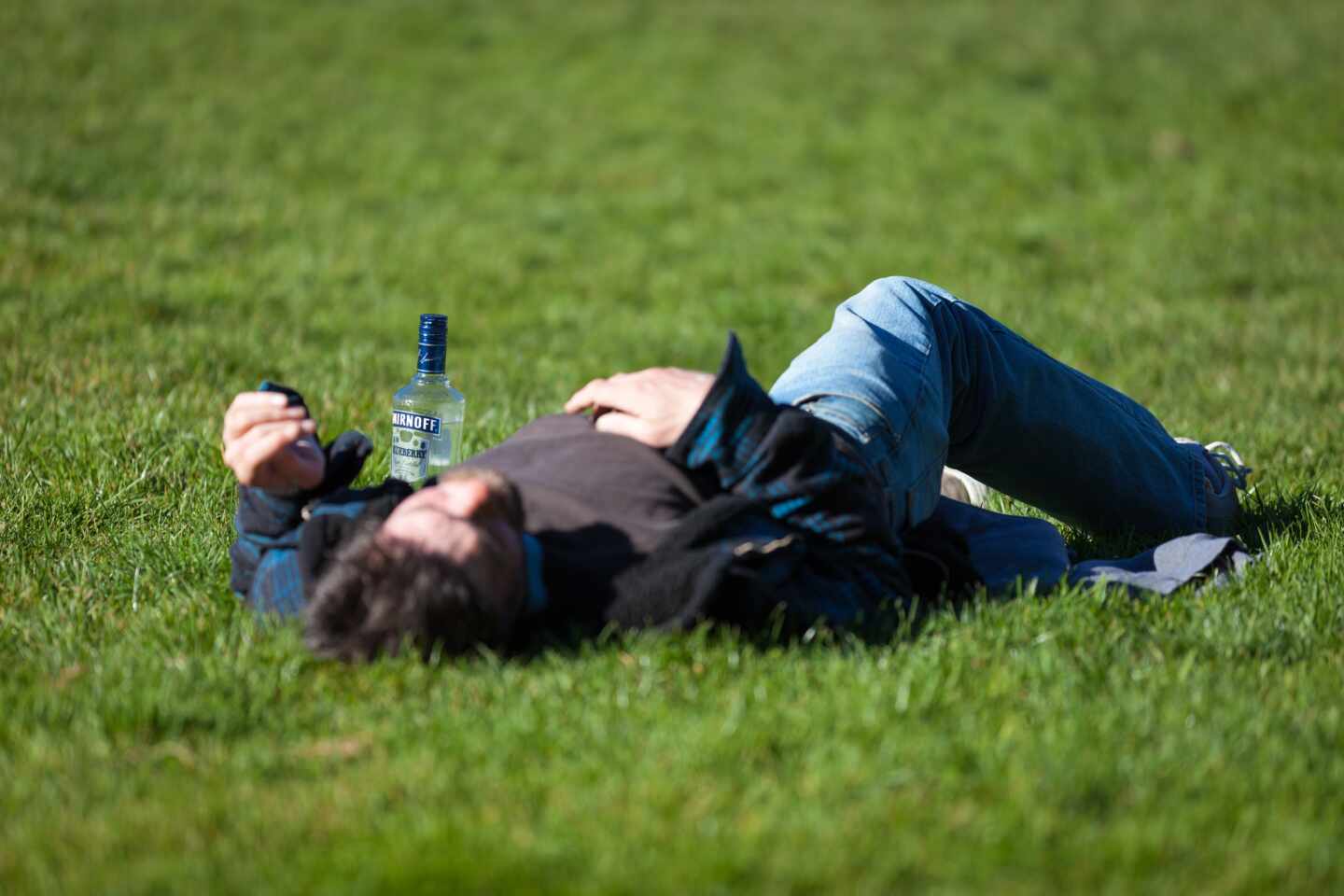 Una persona tumbada en el césped bebiendo alcohol