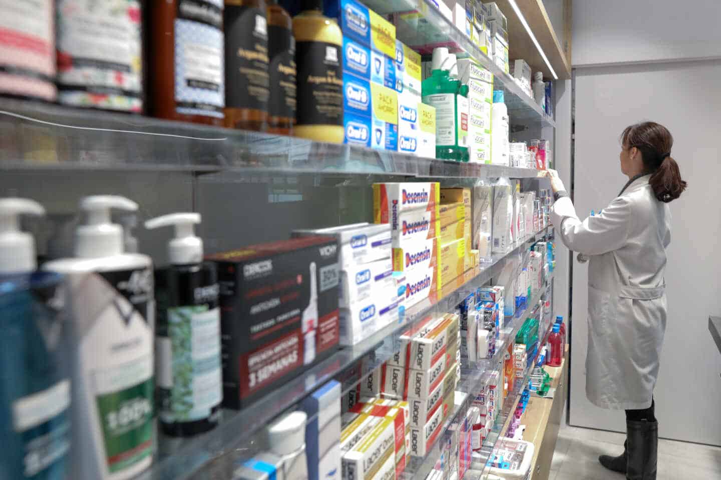 Estante de farmacia con medicamentos, anticonceptivos y antiinflamatorios, y una profesional sanitaria