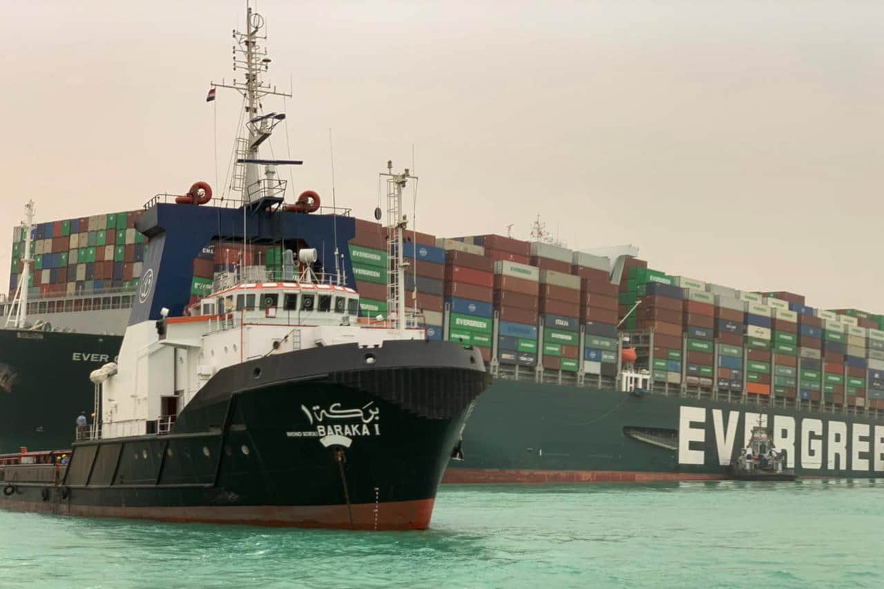 Un remolcador pasa junto al buque portacontenedores llamado Ever Given, operado por Evergreen Marine, encallado en el Canal de Suez.