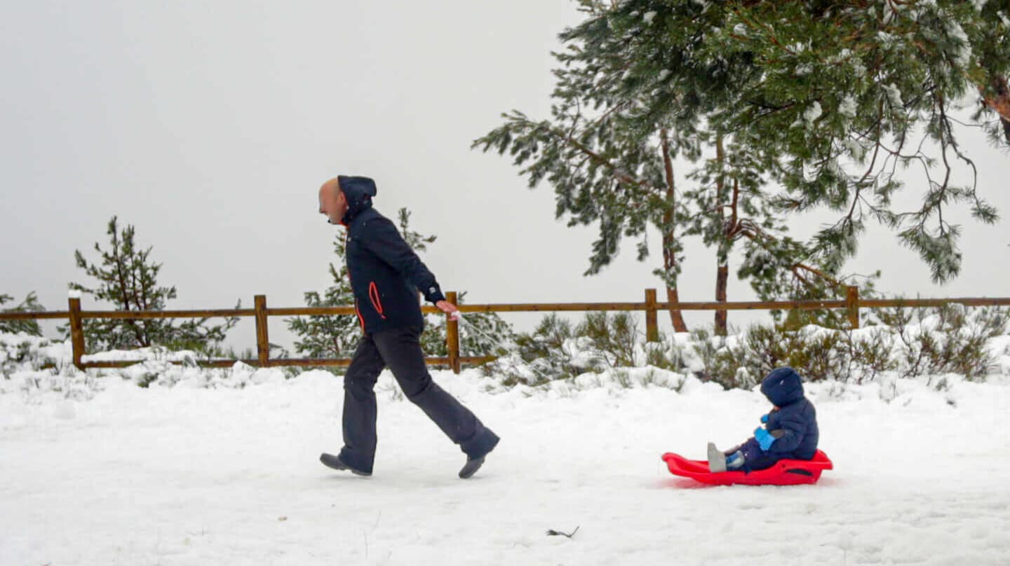 Un padre tira del trineo de su hijo durante el temporal de nieve en la Sierra de Madrid, en el Puerto de Navacerrada