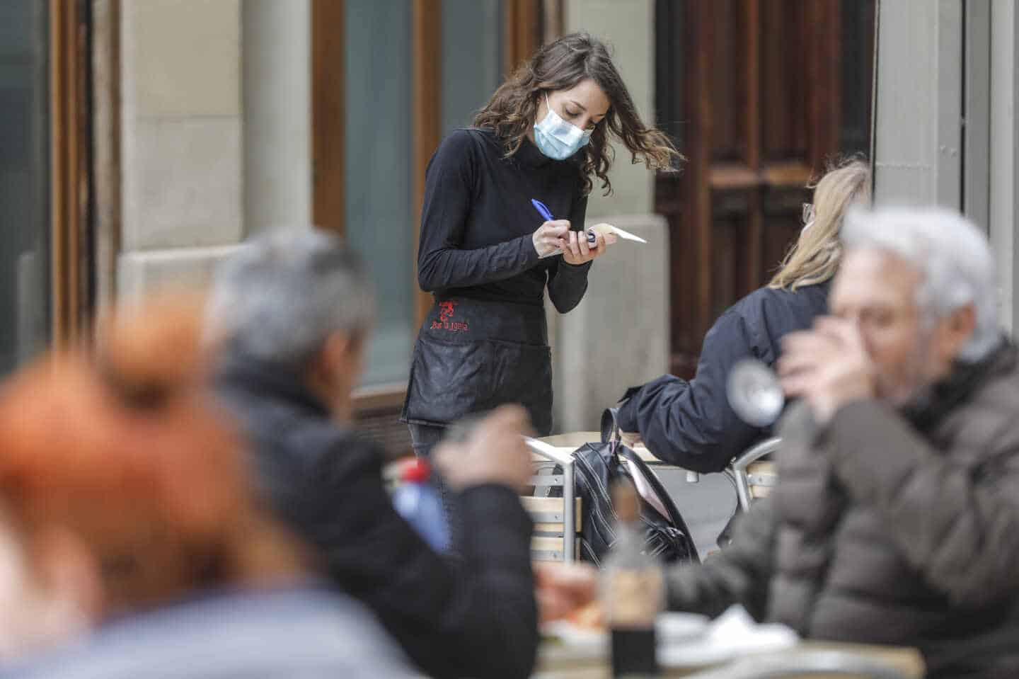 Una camarera atiende a varios clientes en una terraza