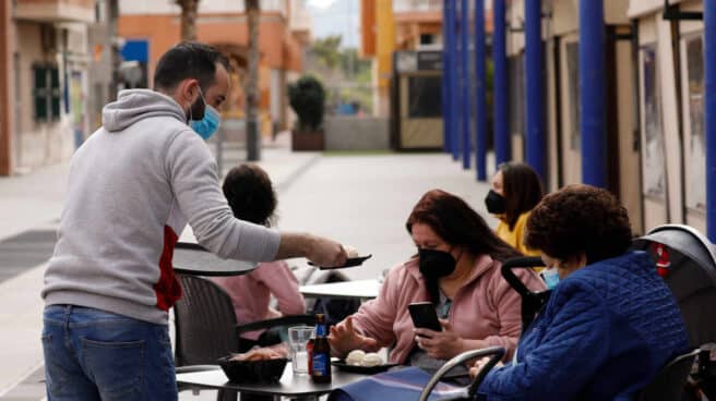 Un camarero atiende a dos clientas en la terraza de un bar.