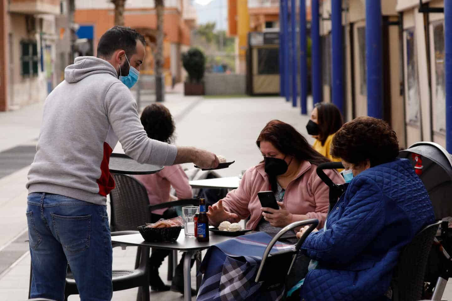 Un camarero atiende a dos clientas en la terraza de un bar.