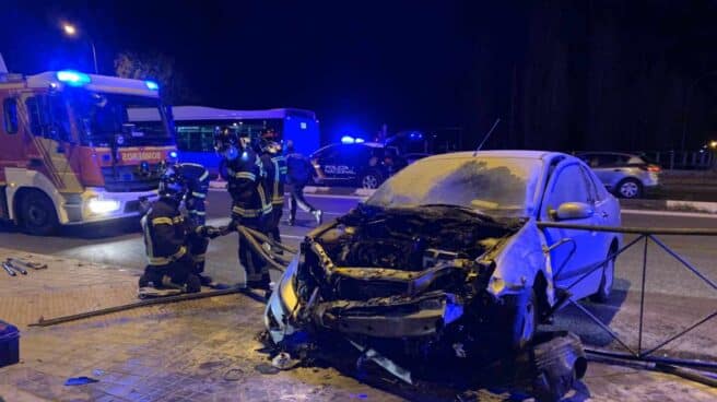 Un coche se incendia tras chocar con una valla en Madrid Los bomberos junto al vehículo calcinado