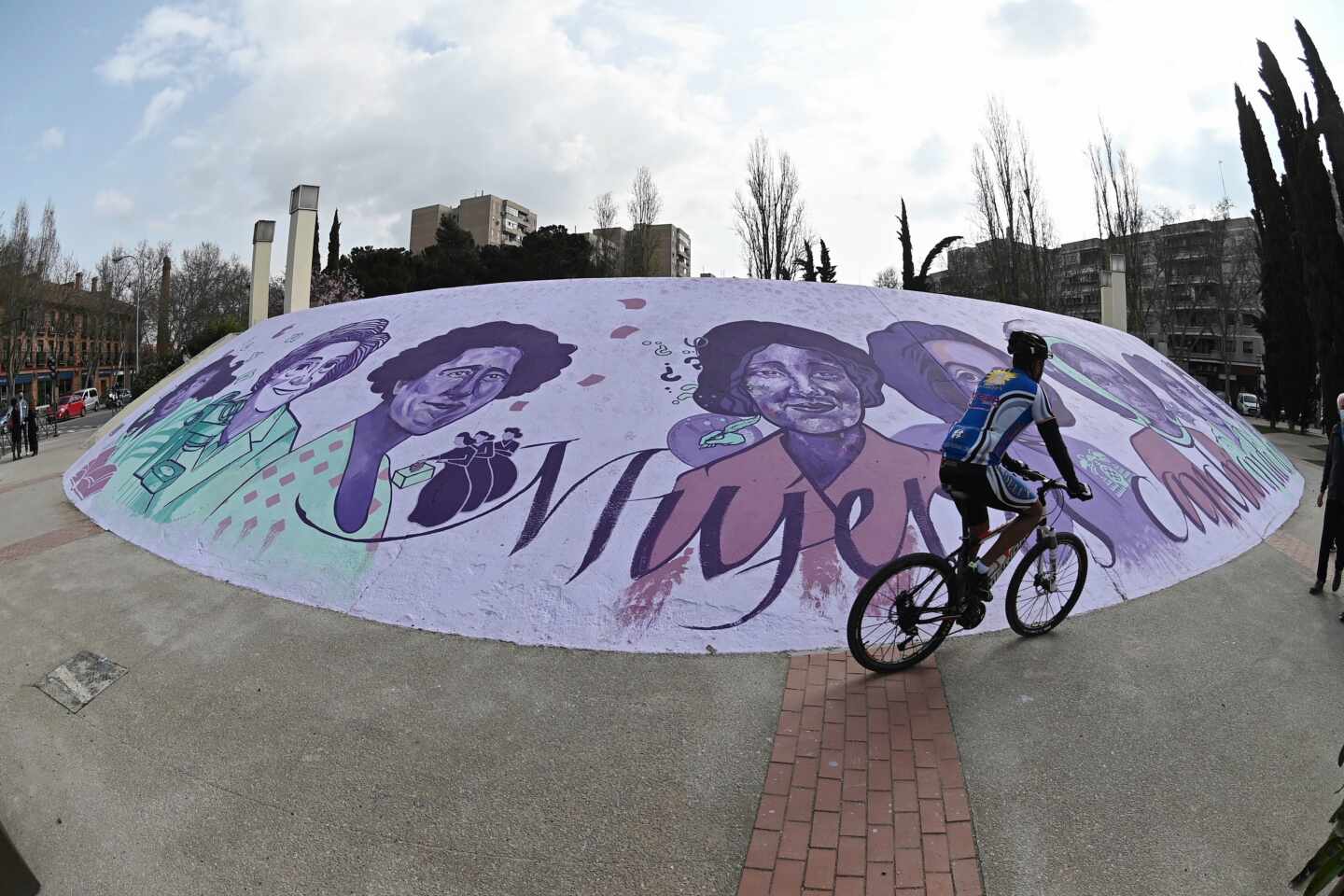 Un ciclista pasa ante el mural feminista al aire libre situado en el paseo de Pastrana de Alcalá de Henares