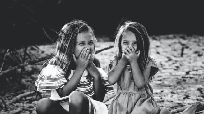 ninas-hablar-sexualidad-psicomami Dos niñas sonríen con las manos en la boca.