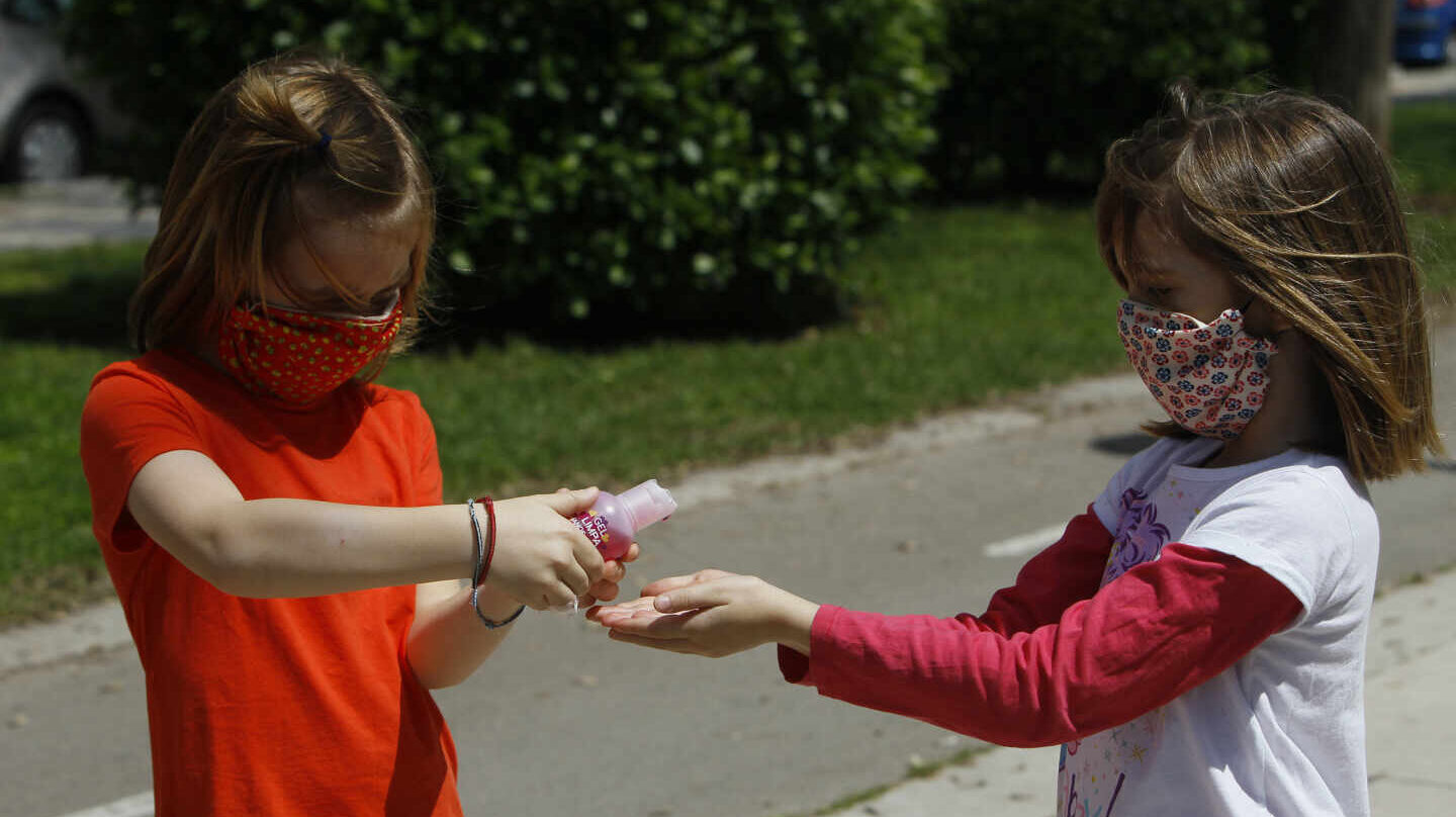 Dos niñas con mascarillas se limpian las manos