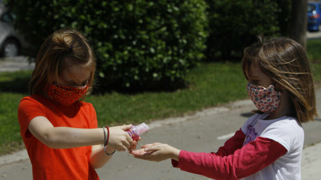 Las mascarillas dejarán de ser obligatorias en los patios de los colegios de Madrid Dos niñas con mascarillas se limpian las manos