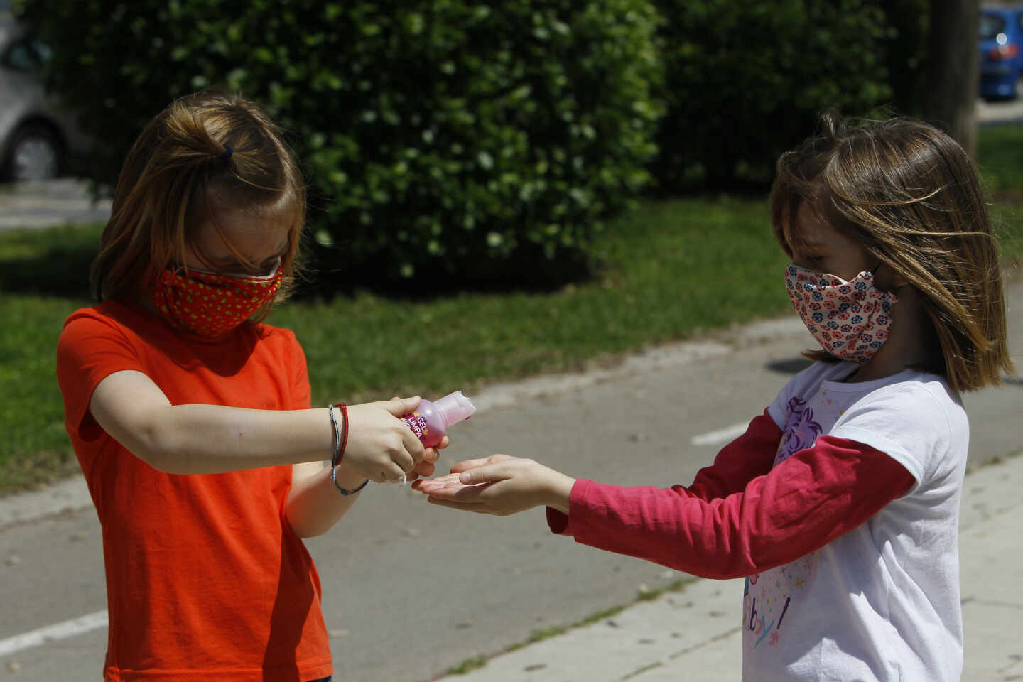 Dos niñas con mascarillas se limpian las manos