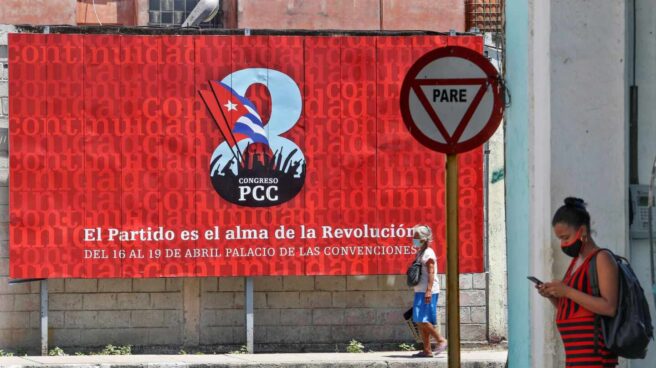 La vida está en la calle. La patria, también Una cubana consulta el móvil ante un cartel sobre el VIII Congreso del Partido Comunista de Cuba