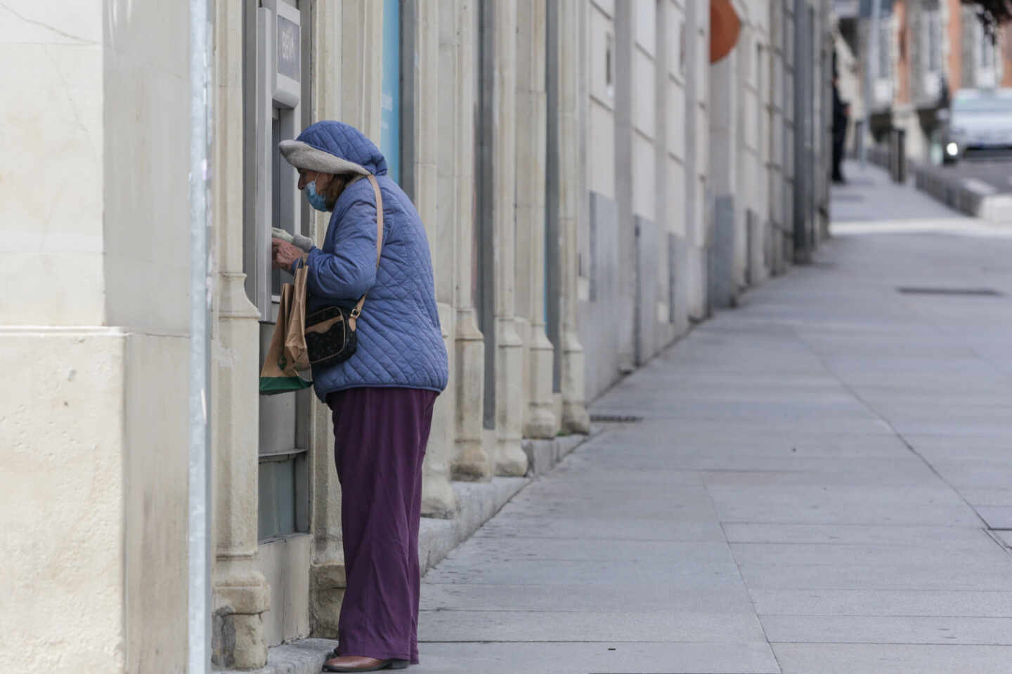 Una mujer protegida con mascarilla y abrigada saca dinero de un cajero.