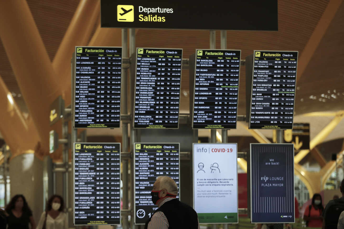 Pasajeros junto a paneles de información en la Terminal T4 del aeropuerto Adolfo Suárez Madrid-Barajas, en Madrid