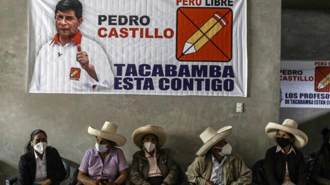 Varios peruanos está sentados bajo un cartel electoral de Pedro Castillo