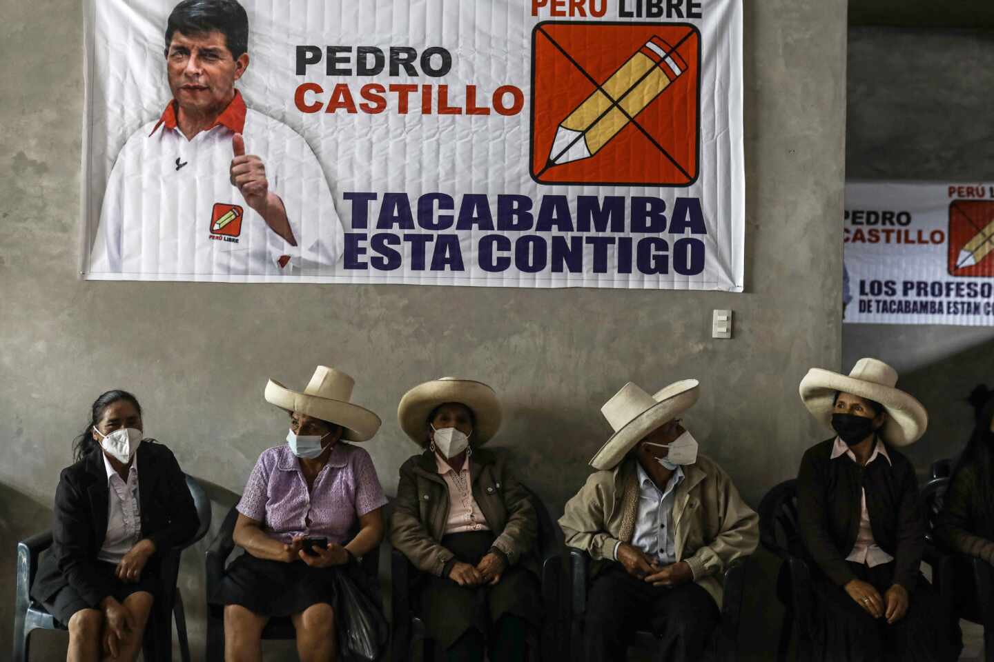Varios peruanos está sentados bajo un cartel electoral de Pedro Castillo