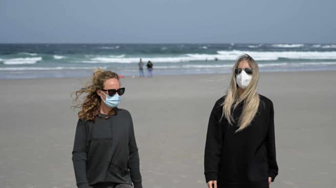 Dos mujeres, con mascarilla en la playa.
