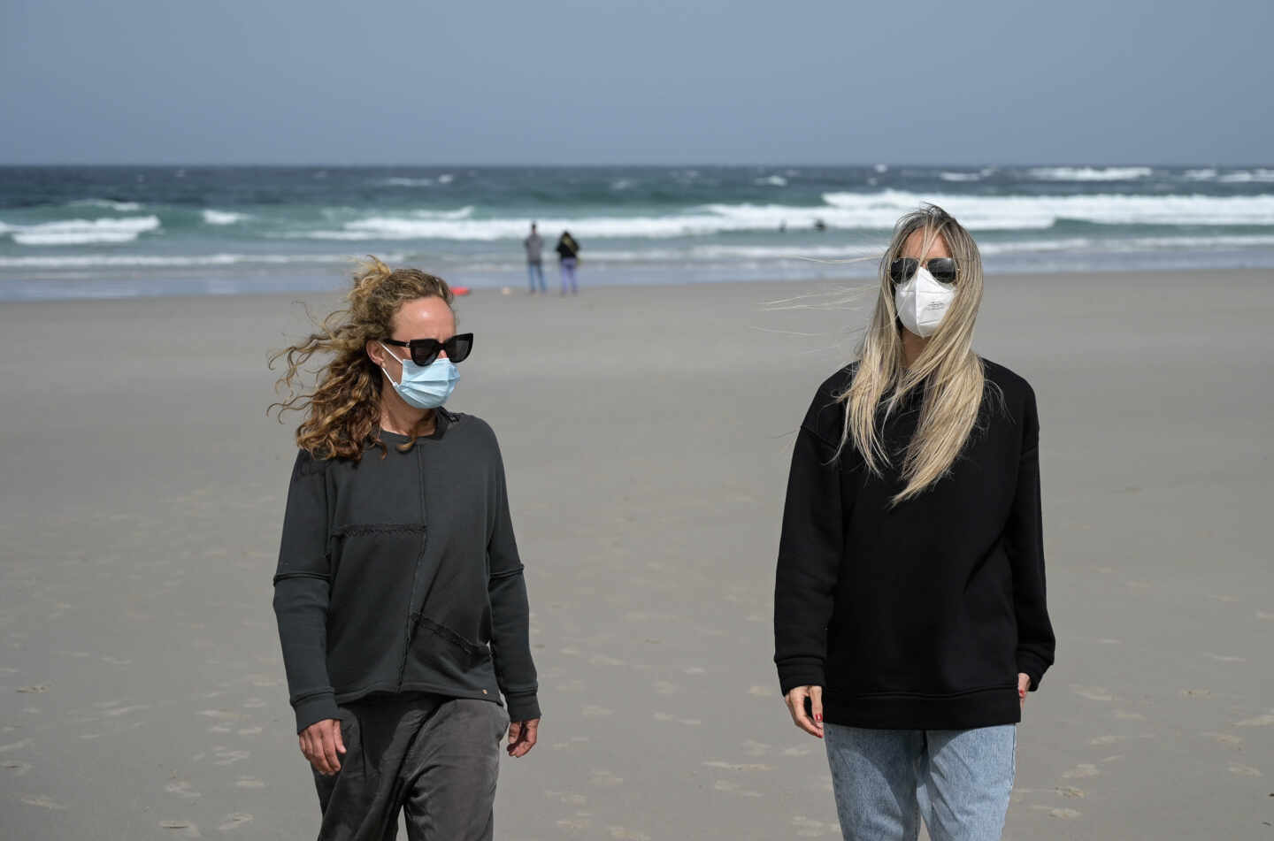 Dos mujeres, con mascarilla en la playa.