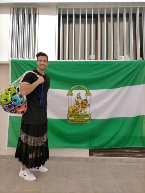 Imagen del profesor con falda junto a la bandera de Andalucía