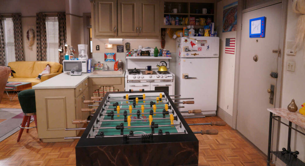 Imagen del apartamento de solteros de Joey y Chandler con el futbolín en primer plano y la cocina americana de fondo