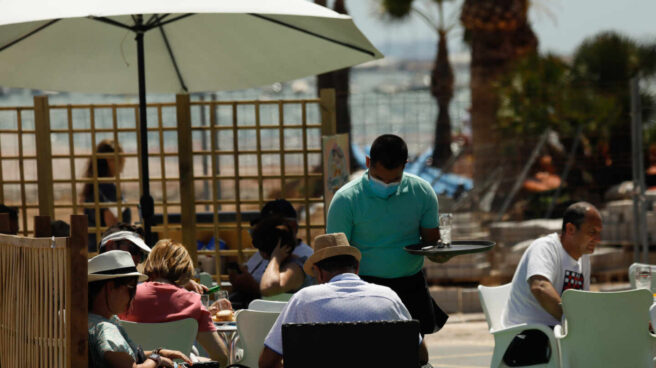 Varias personas en la terraza de un bar, frente a una playa.