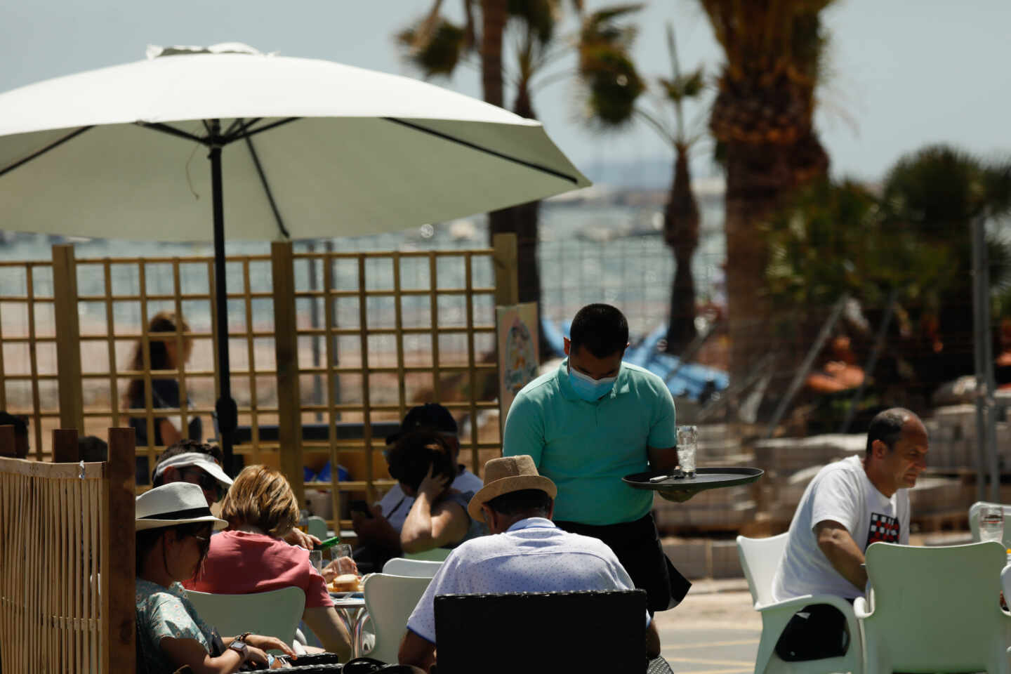 Varias personas en la terraza de un bar, frente a una playa.