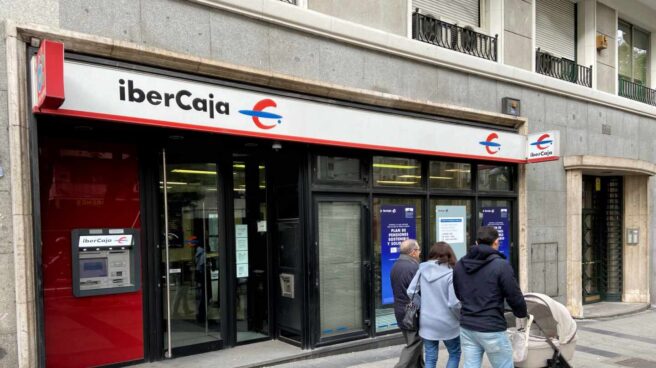 Una familia pasea junto a una oficina de IberCaja en Madrid.