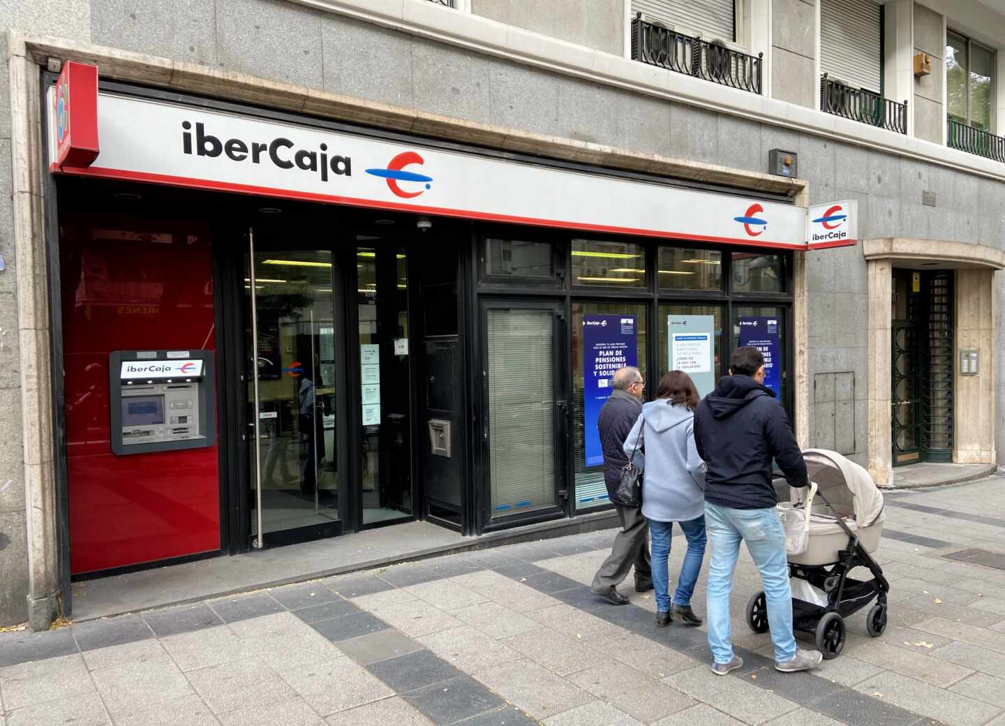 Una familia pasea junto a una oficina de IberCaja en Madrid.