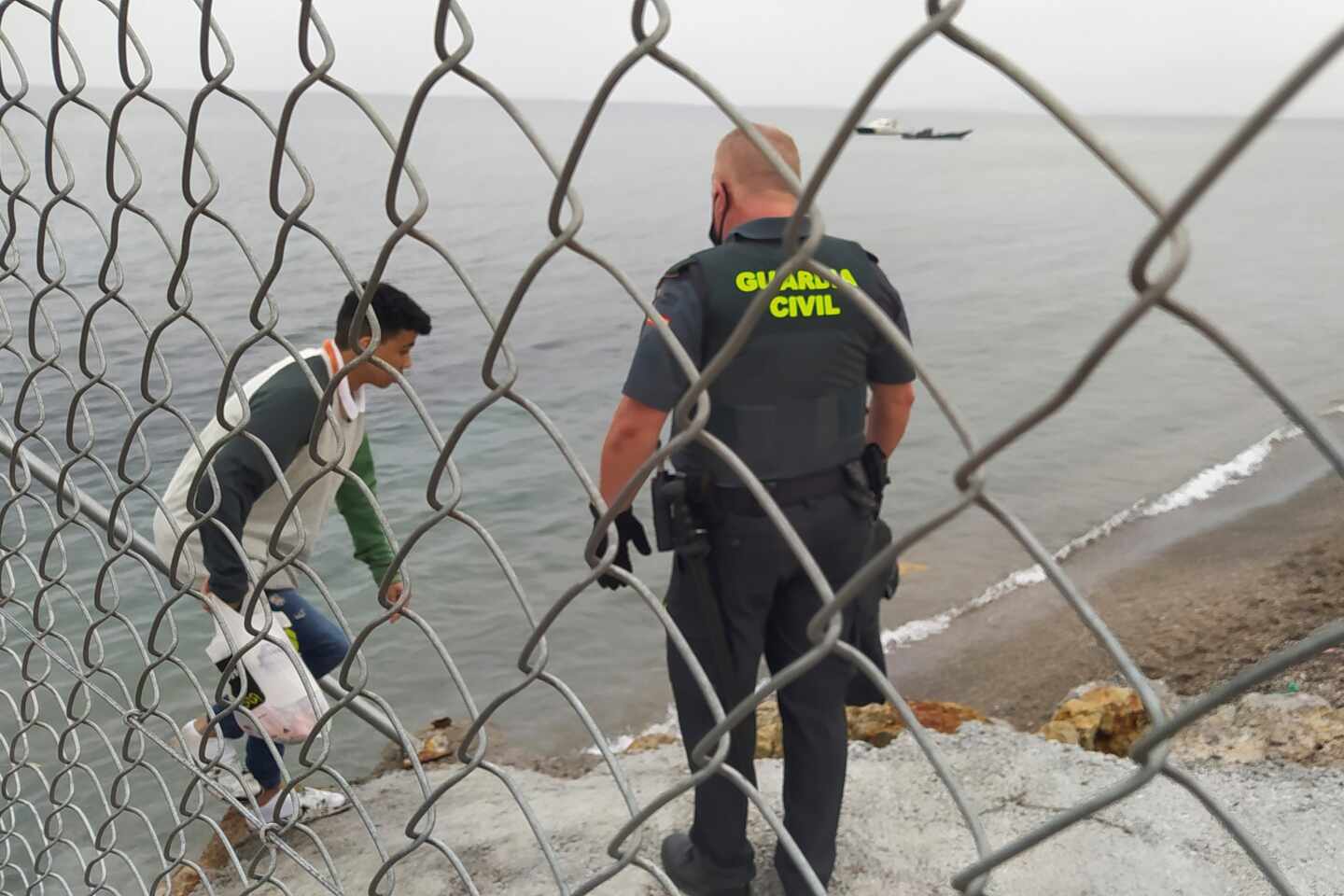 Un Guardia Civil ayuda a uno de los inmigrantes en uno de los espigones fronterizos de Ceuta