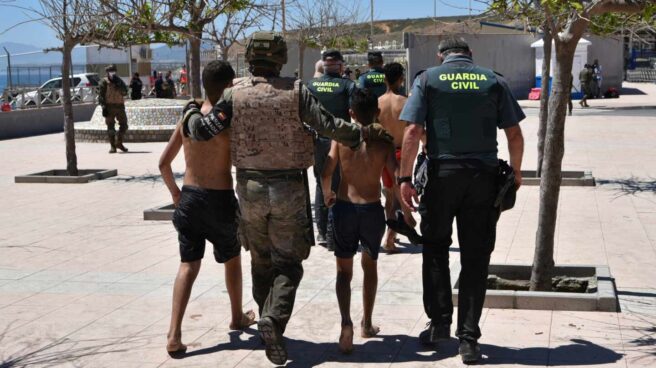 Un militar y un agente de la Guardia Civil ayudan a dos menores migrantes llegados a Ceuta desde Marruecos.