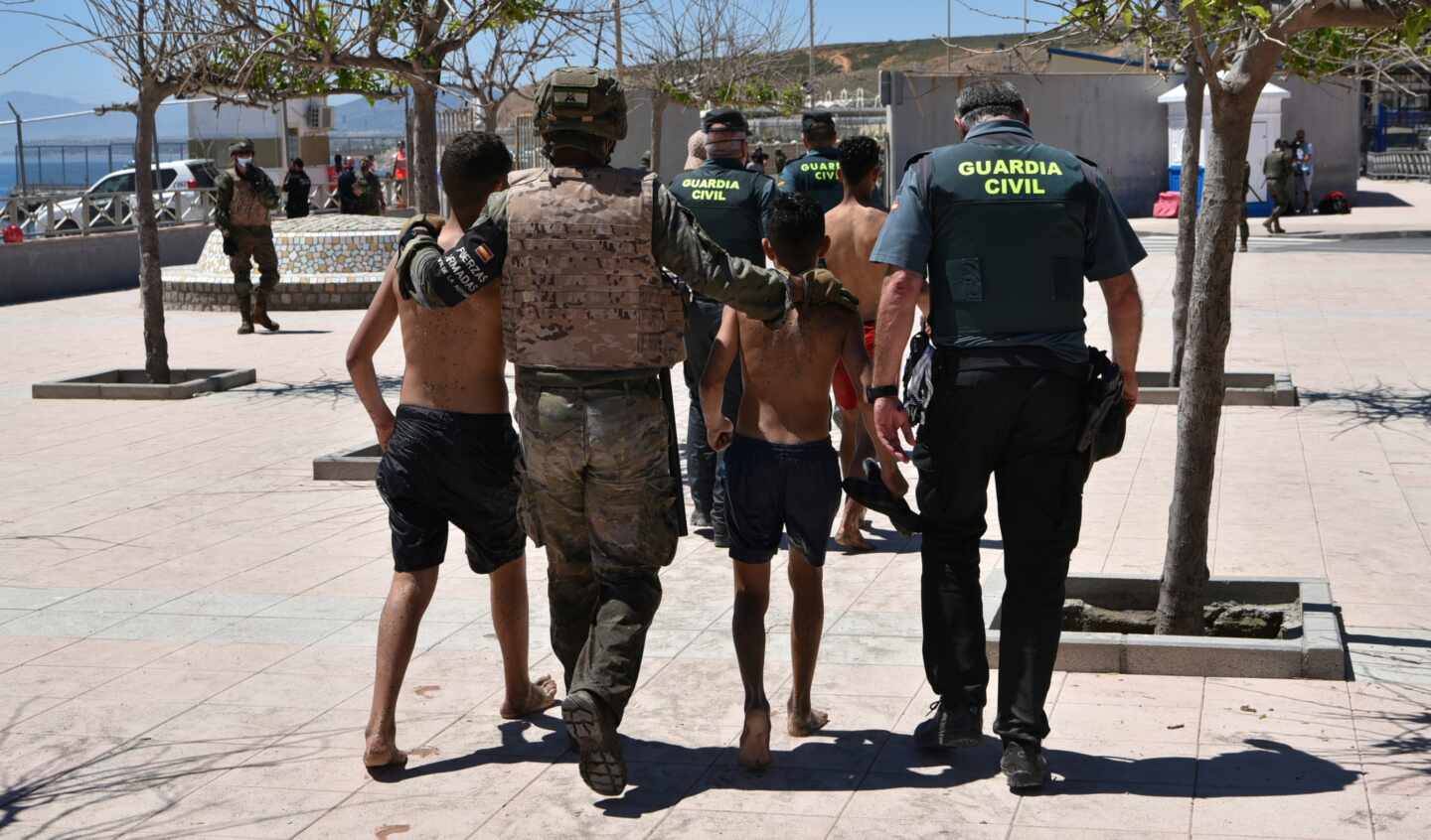 Un militar y un agente de la Guardia Civil ayudan a dos menores migrantes llegados a Ceuta desde Marruecos.