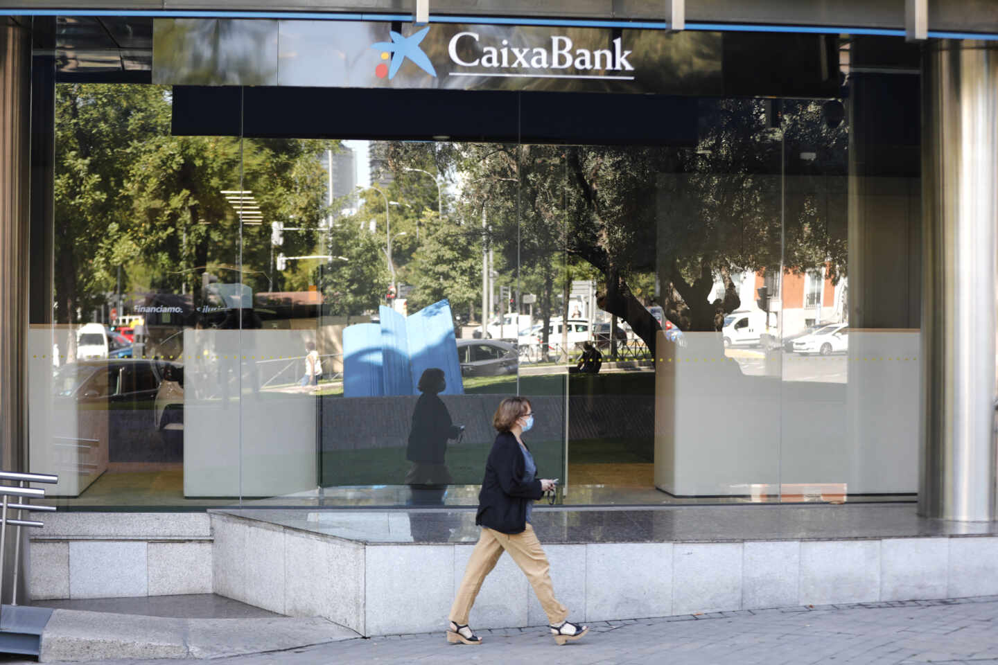 Una mujer pasa por al lado de las oficinas de Caixabank en el Paseo Castellana, en Madrid (España)