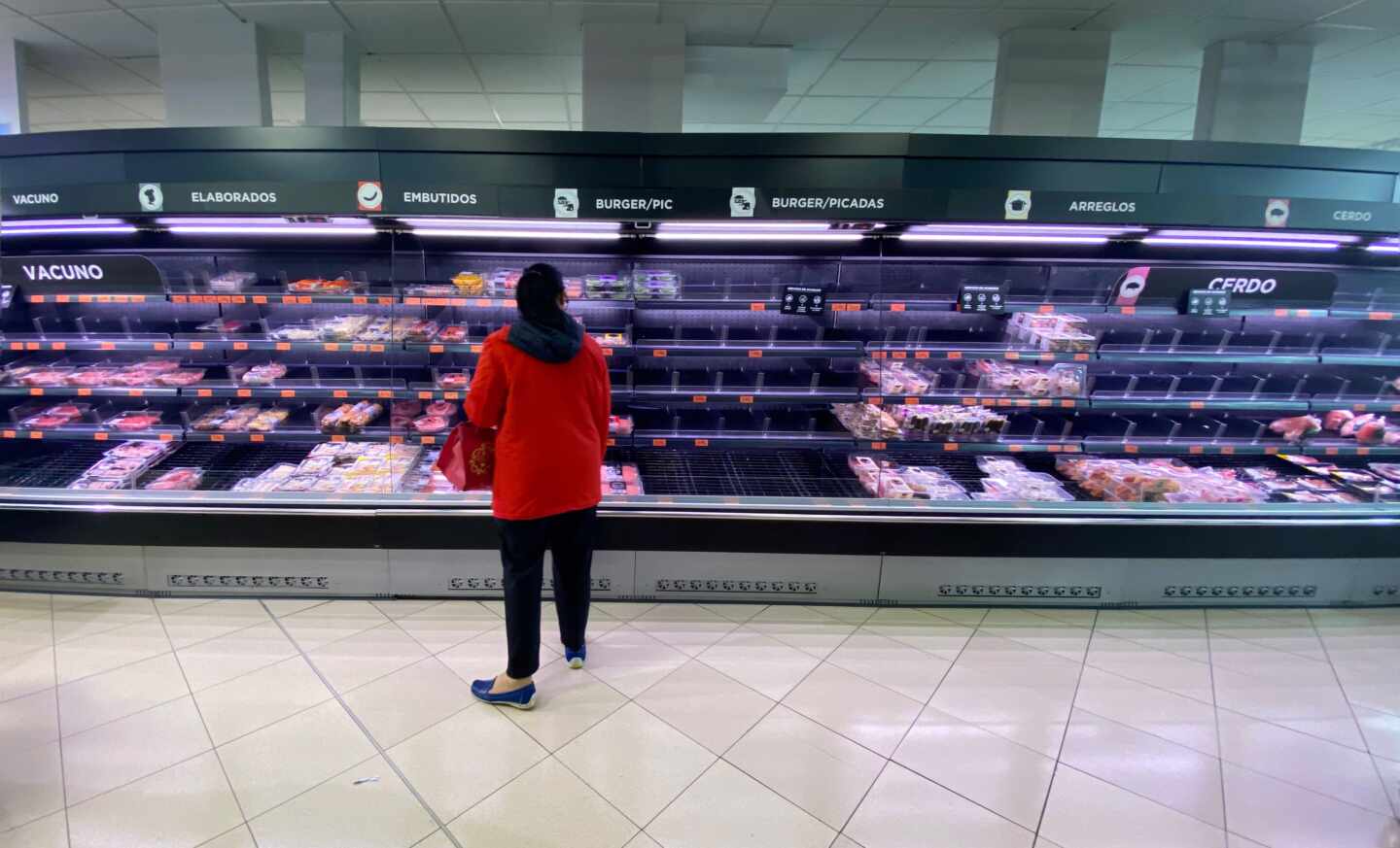 Una mujer observa los alimentos que quedan en los refrigeradores de carne de un supermercado un día marcado por colas de gente deseosas de hacer acopio de alimentos y otros productos debido al avance del coronavirus.