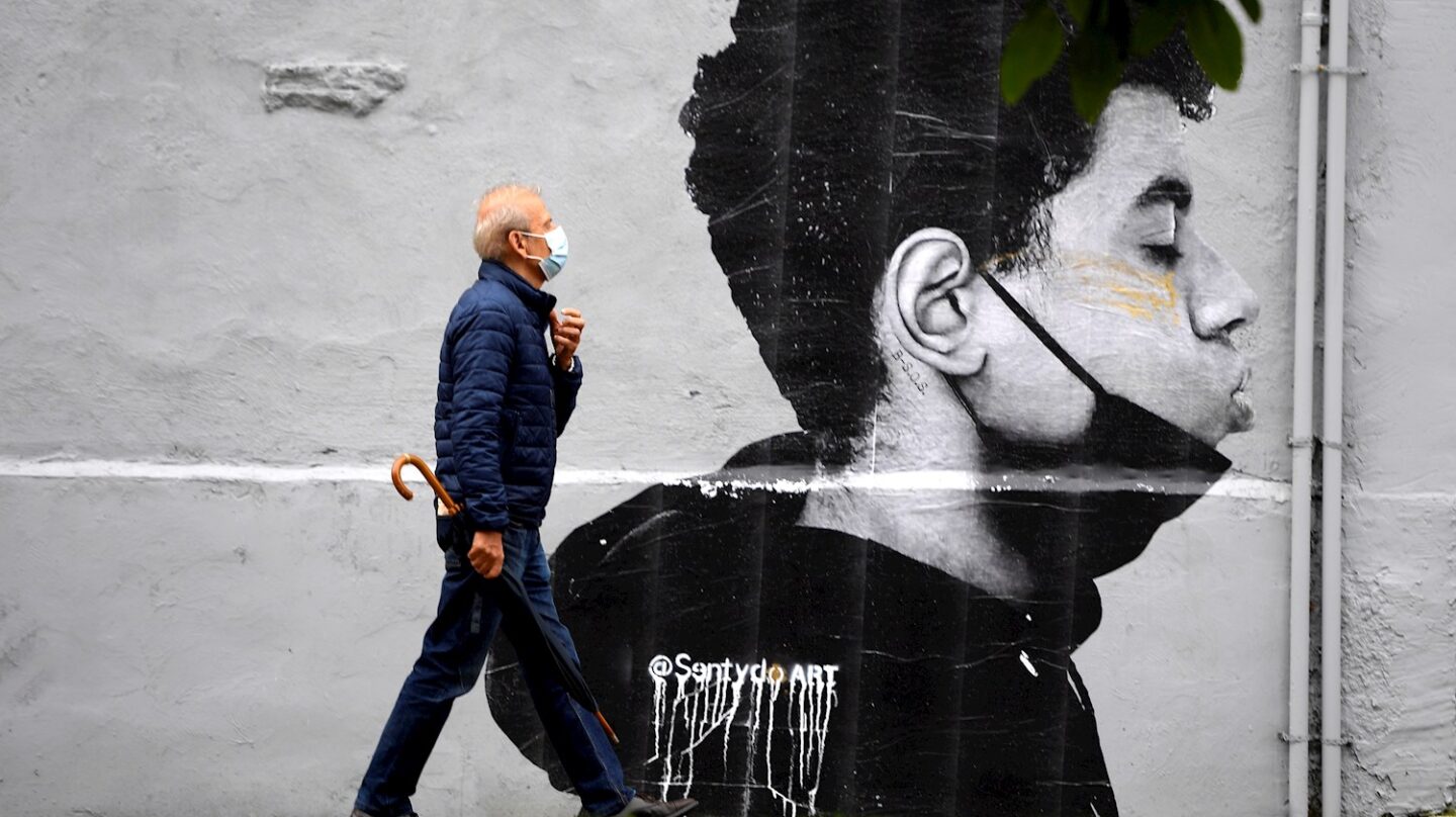 Un hombre camina con mascarilla el primer día sin mascarilla obligatoria en exteriores. Lo hace delante de una obra del artista @Sentydo ART en una campaña dedicada a los besos sin mascarillas.