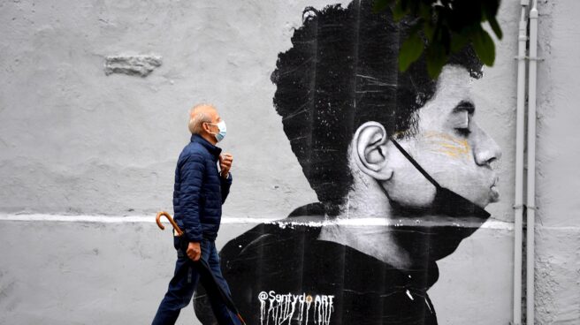 Un hombre camina con mascarilla el primer día sin mascarilla obligatoria en exteriores. Lo hace delante de una obra del artista @Sentydo ART en una campaña dedicada a los besos sin mascarillas.