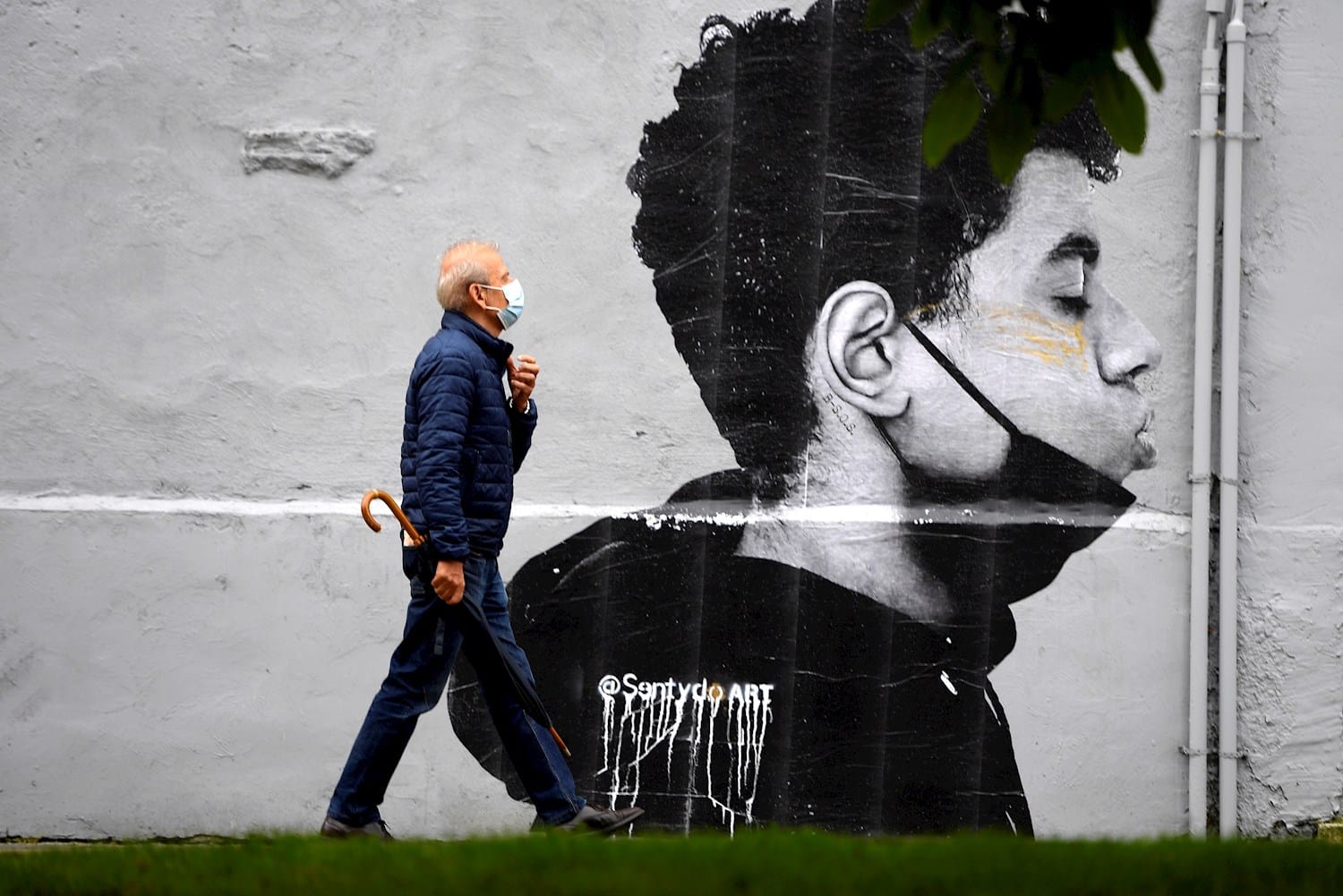 Un hombre camina con mascarilla el primer día sin mascarilla obligatoria en exteriores. Lo hace delante de una obra del artista @Sentydo ART en una campaña dedicada a los besos sin mascarillas.