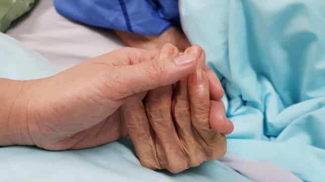 Imagen de un primer plano de dos manos entrelazadas en una cama de hospital