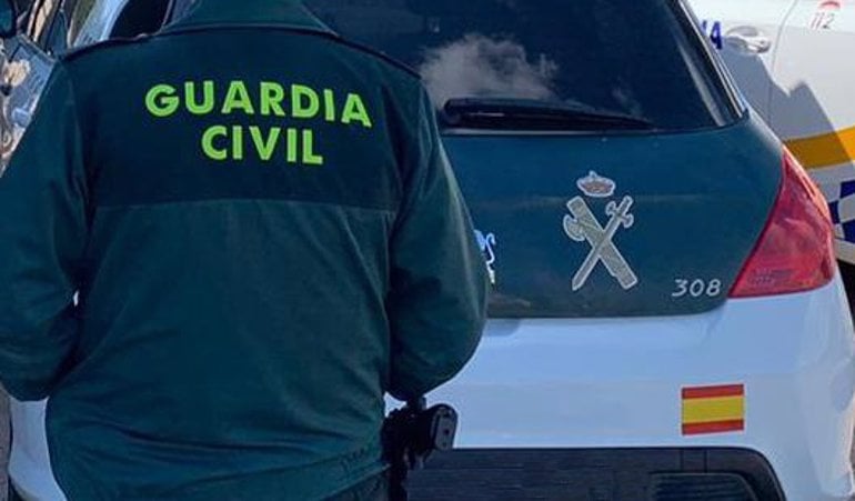 Un agente de la Guardia Civil de espaldas y junto a un vehículo oficial del Cuerpo.