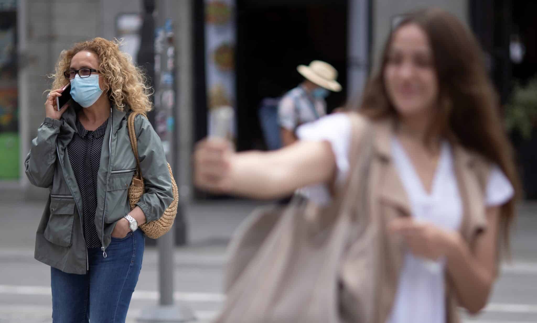 Una chica se hace un selfie en la Puerta del Sol de Madrid ante una mujer con mascarilla.